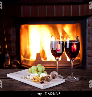 Romantisches Stilleben am Kamin. Gläser Wein, Käse und Nüssen. Stockfoto