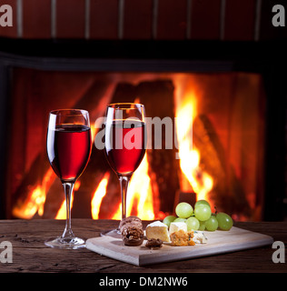 Romantisches Stilleben am Kamin. Gläser Wein, Käse und Nüssen. Stockfoto