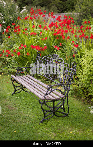 Verzierten Sitzbank in Applecross Garten mit rote Crocosmia blühen im Rahmen Stockfoto