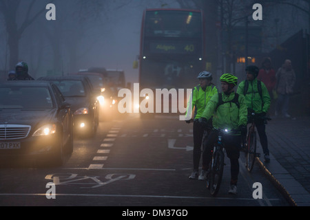 Pendeln Radfahrer warten, um eine Kreuzung überqueren in der Morgendämmerung an einem nebligen Morgen in Südlondon. Stockfoto