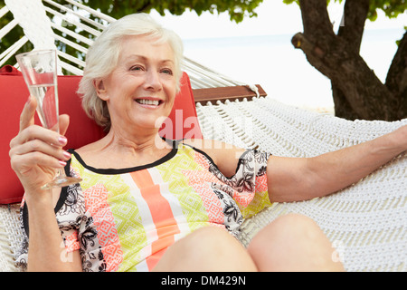 Senior Woman Relaxing In Beach-Hängematte mit Champagner Stockfoto