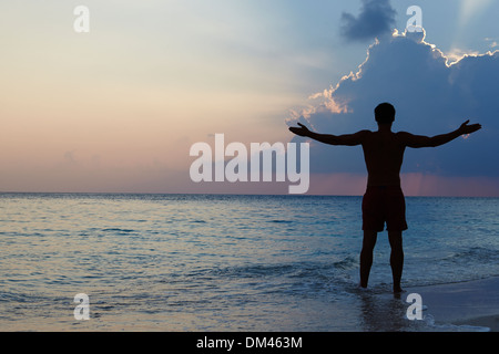 Silhouette der Mann mit ausgestreckten Armen am Strand bei Sonnenuntergang Stockfoto