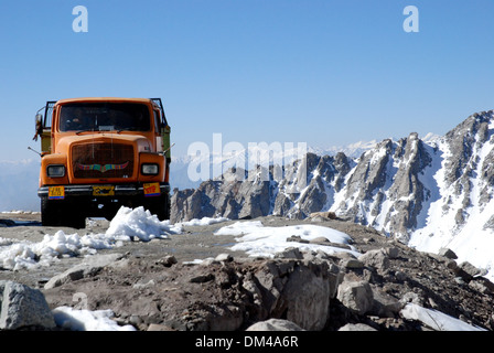 Ladakh, Indien - Juli 2009: eine orange LKW auf großer Höhe kurvenreiche Straße vor schneebedeckten Bergen Stockfoto