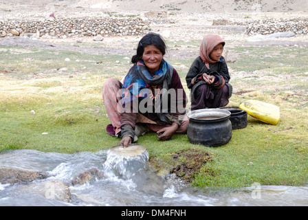 Ladakh, Indien - Juli 2009: eine nomadische Changpa Frau Geschirr spülen neben einem Kind in einem Gebirgsbach in der Nähe von Tso Moriri See. Stockfoto