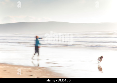 Verschwommenes Bild der Dame throwing Stick für einen Hund auf Sandstrand, Woolacombe, England, UK Stockfoto