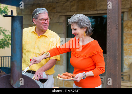 Älteres paar Vorbereitung ein Barbecue auf der Rückseite ihrer Heimat, Texas, USA. Frau setzt die Würstchen auf dem Grill. Stockfoto