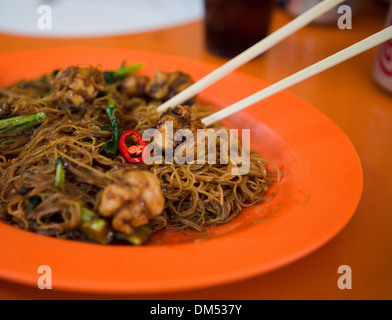 Mittagessen in Maxwell Road Hawker Centre - sehr feine Nudeln mit rotem Chili und Schweinefleisch, auf einem hellen orange Teller mit Stäbchen. Stockfoto