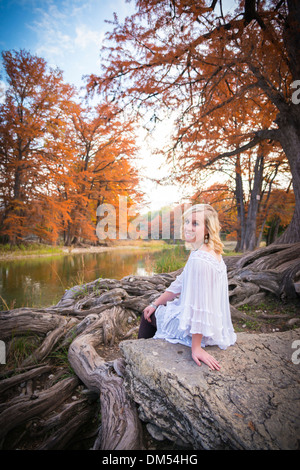 Kaukasischer weibliche Teenager sitzt auf einem Felsen neben Cypress Baumwurzeln und genießen der Natur am Fluss Frio. Stockfoto