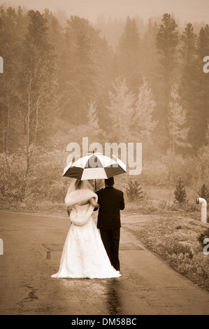 Braut und Bräutigam zu Fuß in den Regen unter Dach Stockfoto