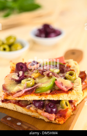 Frische hausgemachte Pizza-Stücke mit Tomatensauce, Schinken, Salami, Oliven, Paprika und Käse auf der Oberseite auf Holzbrett mit Messer Stockfoto