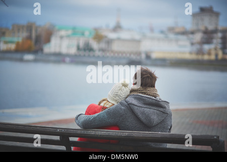 Rückansicht des liebevollen paar auf der Bank sitzen und mit Blick auf Fluss Stockfoto