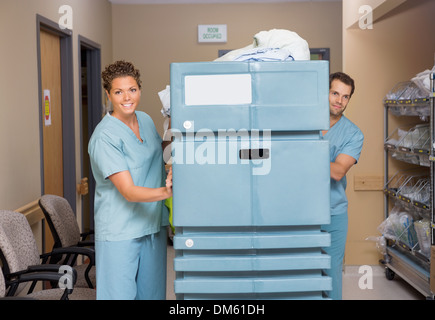 Krankenschwestern drängen Trolley gefüllt mit Leinen In Krankenhaus-Flur Stockfoto