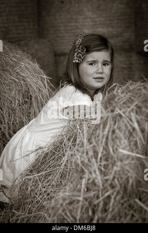 Junges Mädchen im weißen Kleid unter Heu Ballen in einer Scheune. Stockfoto