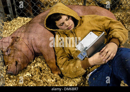10. Februar 2005; San Antonio, TX, USA; CODY JANDT, 12, Seguin, Texas und entspannt mit seinem Schwein '' Big Red'' in einem Stift an der Schweine-Scheune auf dem Gelände der San Antonio Stock Show und Rodeo auf Donnerstag, 10. Februar 2005. Jandt verging die Zeit den Film "Peter Pan" auf seiner tragbaren DVD-Player. Stockfoto