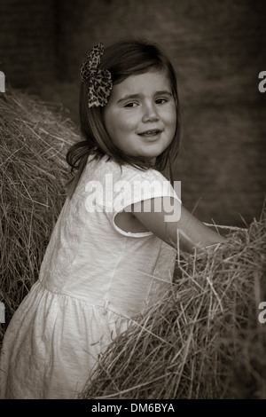 Junges Mädchen im weißen Kleid unter Heu Ballen in einer Scheune. Stockfoto