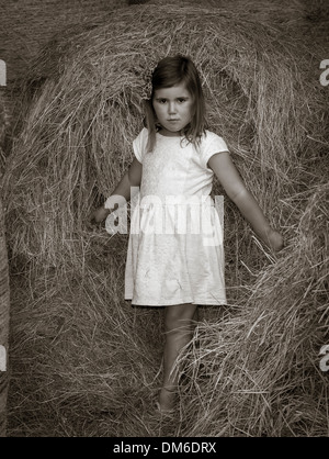 Junges Mädchen im weißen Kleid unter Heu Ballen in einer Scheune. Stockfoto