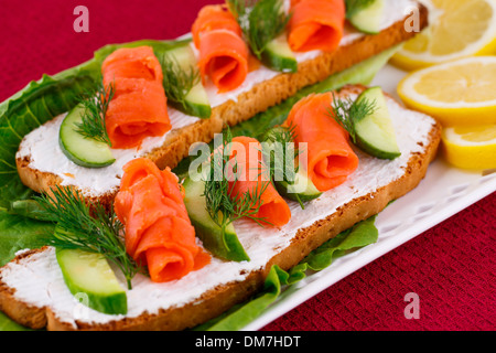 Lachs Sandwiches mit Salat, frische und eingelegte Gurken, Zwiebel, Zitrone auf Platte. Stockfoto