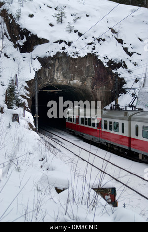 Zug in Richtung einen kurzen Tunnel unter eine große Felsformation an einem verschneiten Wintertag Stockfoto