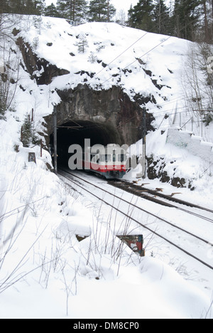 Zug in Richtung einen kurzen Tunnel unter eine große Felsformation an einem verschneiten Wintertag Stockfoto