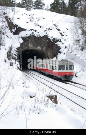 Zug in Richtung einen kurzen Tunnel unter eine große Felsformation an einem verschneiten Wintertag Stockfoto