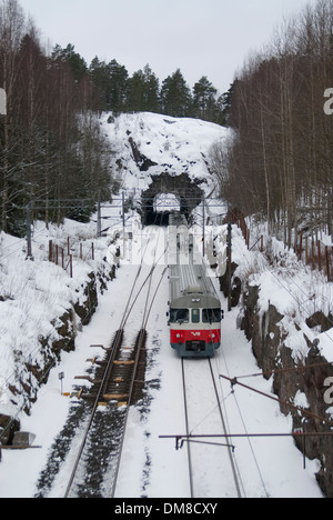 Zug in Richtung einen kurzen Tunnel unter eine große Felsformation an einem verschneiten Wintertag Stockfoto