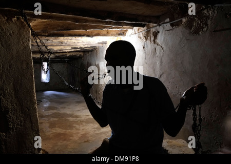 Ein afrikanischer Mann, der einen mit Ketten gebundenen Sklaven im Keller von St. Monica in Stone Town auf der Insel Sansibar, einem halbautonomen Teil Tansanias, in Ostafrika, darstellt. Die Stone Town war Gastgeber eines der letzten offenen Sklavenmärkte der Welt, dem arabische Händler bis zur Schließung durch die Briten im Jahr 1873 vorstanden. Stockfoto