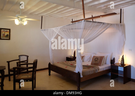 Bett mit Moskitonetz Baldachin in einem Zimmer im Diamonds Mapenzi Beach Hotel an der Nordostküste der Insel Sansibar, einem halb autonomen Teil von Tansania, in Ostafrika Stockfoto