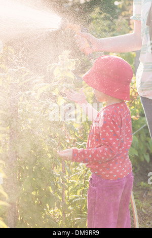 Lifestyle Sommer-Szene. Kleine Mädchen spielen mit Eltern im Garten, Gefühl Wasser aus Sprinkleranlagen Stockfoto