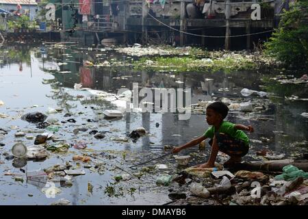 Phnom Penh, Kambodscha. 10. Dezember 2013. Ein Junge spielt in einer Pfütze aus einer Überschwemmung im Chhba Anmpov Slum auf dem Gelände einer chinesischen Friedhof in Phnom Penh, Kambodscha, 10. Dezember 2013. UNICEF unterstützt die lokalen Projekt "Mith Samlanh" (beleuchtet: Freunde), die kümmert sich um die Kinder. Kambodscha ist eines der 20 Länder mit den höchsten Raten von Unterernährung bei Kindern. Rund 670.000 Waisenkinder leben in Kambodscha. Jedes 22. Kind stirbt im ersten Jahr des Lebens. Mehr als ein Drittel der Bevölkerung lebt von weniger als einem Dollar pro Tag. Foto: Jens Kalaene/Dpa/Alamy Live News Stockfoto