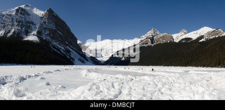 Lake Louise im Winter mit einer dicken Schicht aus Eis & Schnee bedeckt. Menschen zu Fuß auf den See, die Sonne genießen. Stockfoto