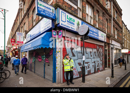 Ein Polizist steht Wache außerhalb eines der vielen Off-Licence-Shops in Londons Brick Lane. Stockfoto