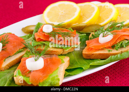 Lachs Sandwiches mit Salat, frische und eingelegte Gurken, Zwiebel, Zitrone auf Platte. Stockfoto