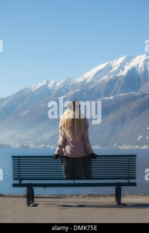 eine Mädchen in einem rosa Mantel sitzt auf einer Bank am See Stockfoto