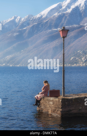 eine Frau in einem rosa Mantel sitzt auf einem Steg am See Stockfoto