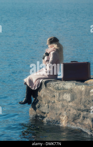 eine Frau in einem rosa Mantel sitzt auf einem Steg am See Stockfoto