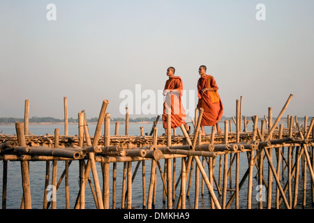 Zwei buddhistische Mönche orange Safron Roben tragen gehen auf eine Bambusbrücke über den Mekong River in Kampong Cham, Kambodscha. Stockfoto