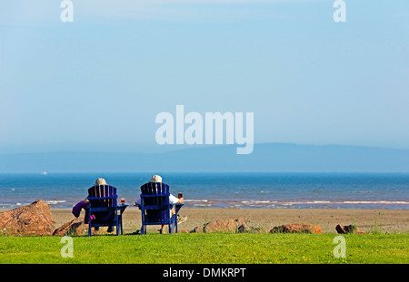 Zwei Menschen sitzen auf blauen Adirondack Liegestühle mit Blick auf den Strand. Stockfoto