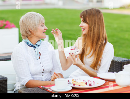 Ältere Mutter und junge attraktive Tochter essen Kuchen, trinken Kaffee im Café, Lächeln Stockfoto