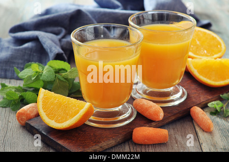 Orange und Karotten-Saft im Glas mit Minze, frisches Obst und Gemüse auf hölzernen Hintergrund Stockfoto