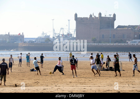 Lokale Marokkaner Fußball spielen am Strand mit Booten und Hafen Skala du Port im Hintergrund essaouira Marokko Stockfoto