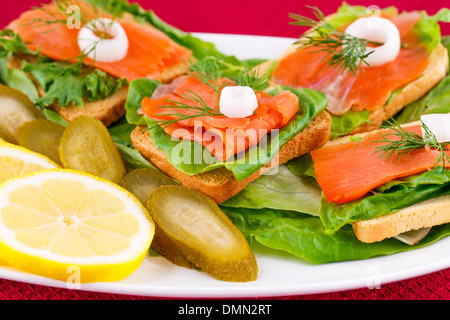 Lachs Sandwiches mit Salat, frische und eingelegte Gurken, Zwiebel, Zitrone auf Platte. Stockfoto