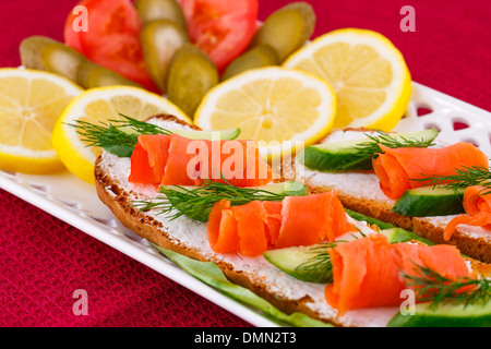 Lachs Sandwiches mit Salat, frische und eingelegte Gurken, Zwiebel, Zitrone auf Platte. Stockfoto