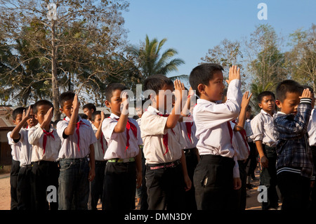 Horizontale Ansicht von Schulkindern salutieren und gemeinsam zu singen, während ihre Fahne heben an einer Schule in Laos. Stockfoto