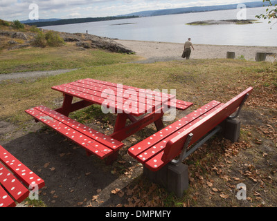 Roten Parkbänke verziert mit weißen Punkten an einem Strand in den Oslo-Fjord in Norwegen, ein Mann zu Fuß in Richtung Ufer Stockfoto