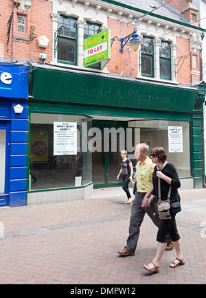 Menschen zu Fuß vorbei an leeren geschlossenen Schuh shop mit lassen Sie Zeichen, Abergavenny, Wales, UK Stockfoto