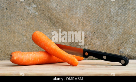 Frische Karotten und Küchenmesser auf Holzbrett. Stockfoto