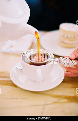 Eine Person, eine Tasse Tee mit einem Sieb gießen. Weißware. Elegante Nachmittagstee. Stockfoto