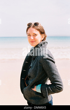 Eine Frau in einem grauen Mantel am Strand. Stockfoto