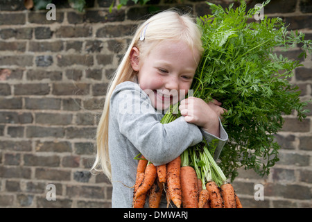 Ein junges Mädchen hält eine große Reihe von Karotten. Stockfoto