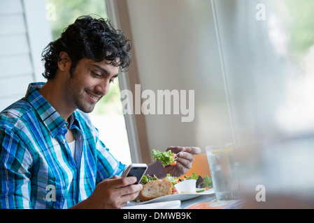 Ein Mann sitzt überprüft seine Telefon und Essen in einem Café. Stockfoto